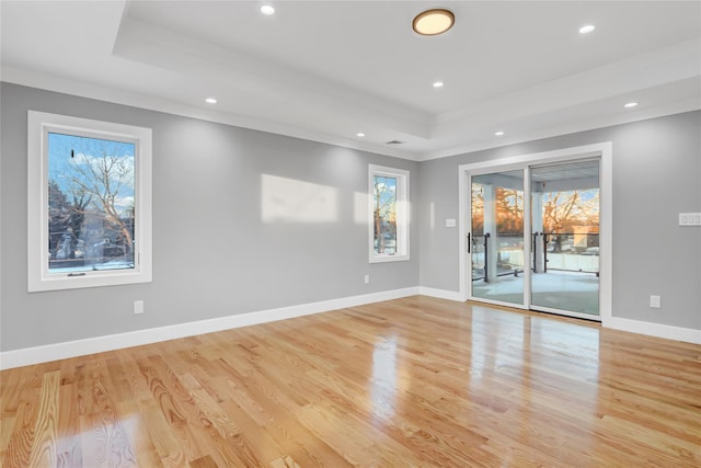 empty room with light hardwood / wood-style floors, a tray ceiling, and ornamental molding