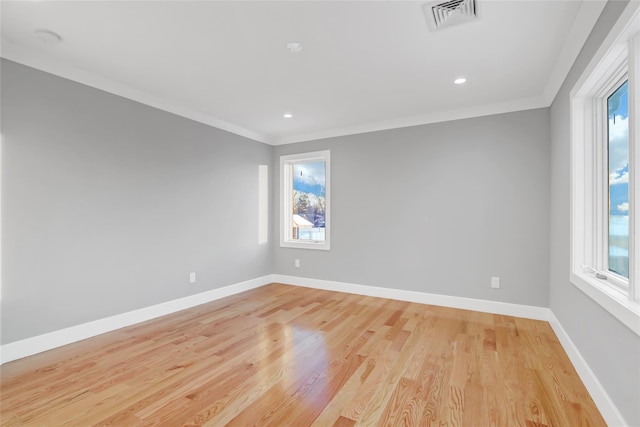 spare room featuring a wealth of natural light, ornamental molding, and light wood-type flooring