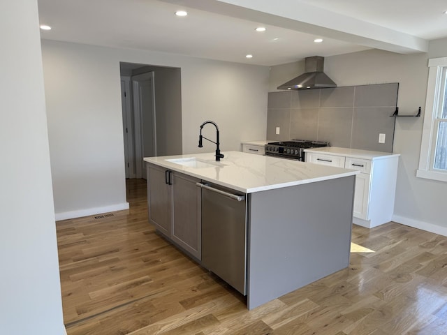 kitchen featuring gray cabinetry, stainless steel appliances, a sink, wall chimney exhaust hood, and a center island with sink