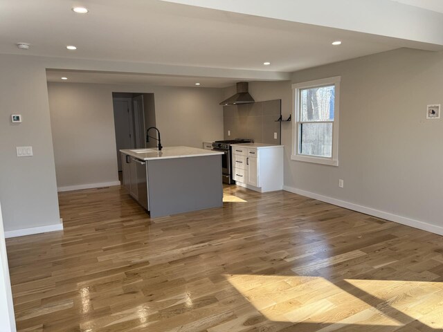 kitchen with a center island with sink, baseboards, wall chimney exhaust hood, appliances with stainless steel finishes, and light countertops