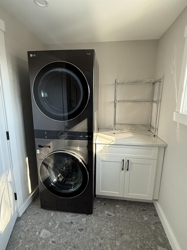 laundry area featuring stacked washing maching and dryer, baseboards, and cabinet space