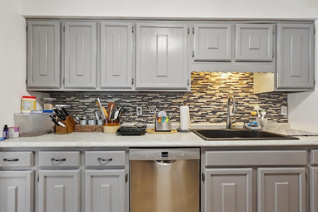 kitchen with light countertops, stainless steel dishwasher, a sink, backsplash, and gray cabinetry