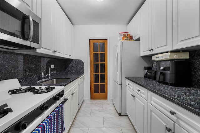 kitchen featuring sink, dark stone countertops, white appliances, decorative backsplash, and white cabinets