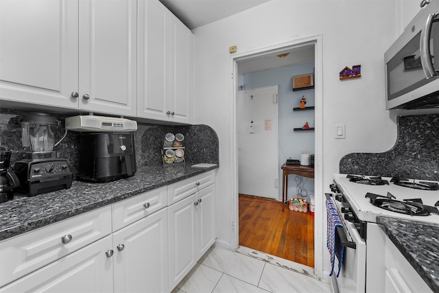 kitchen featuring white cabinetry, dark stone counters, white gas range oven, and decorative backsplash