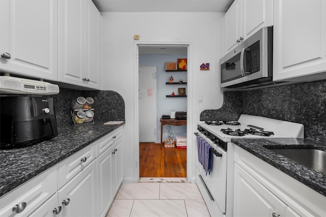 kitchen with tasteful backsplash, dark stone countertops, white gas stove, and white cabinets