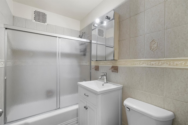 full bathroom featuring tile walls, vanity, toilet, and combined bath / shower with glass door