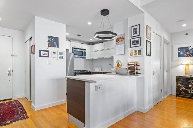 kitchen with white cabinets, appliances with stainless steel finishes, hanging light fixtures, kitchen peninsula, and light hardwood / wood-style flooring