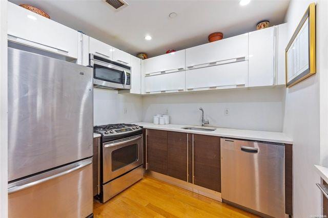 kitchen featuring sink, stainless steel appliances, white cabinetry, and light hardwood / wood-style floors