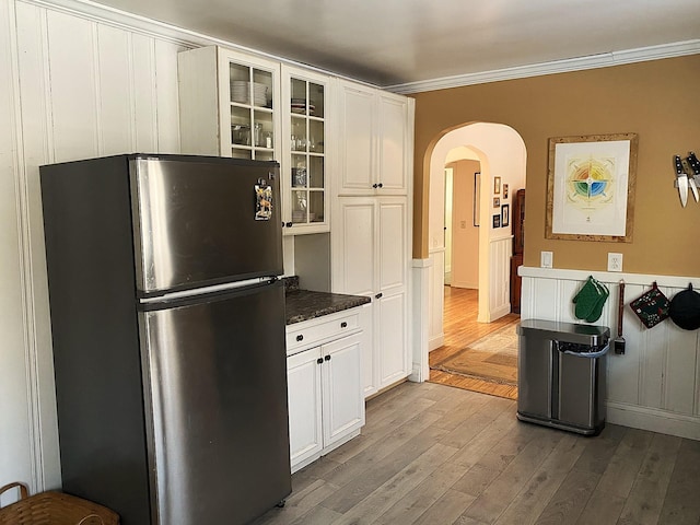 kitchen with white cabinets, light wood-type flooring, ornamental molding, and stainless steel fridge