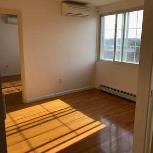 empty room featuring baseboard heating, a wall unit AC, wood finished floors, and baseboards