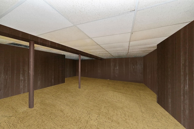 basement with a paneled ceiling and wood walls