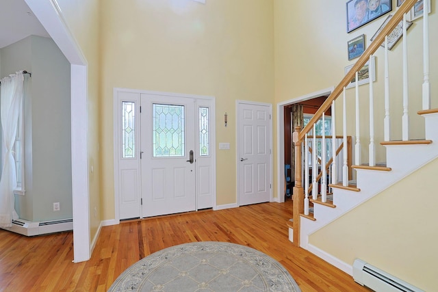 foyer entrance with a baseboard radiator, a high ceiling, and light wood-type flooring