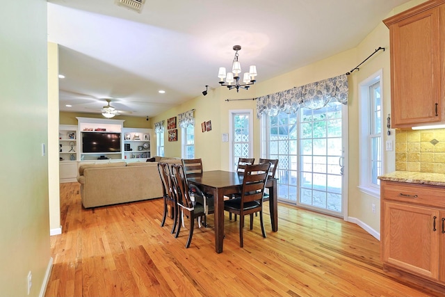 dining space with ceiling fan with notable chandelier and light hardwood / wood-style flooring