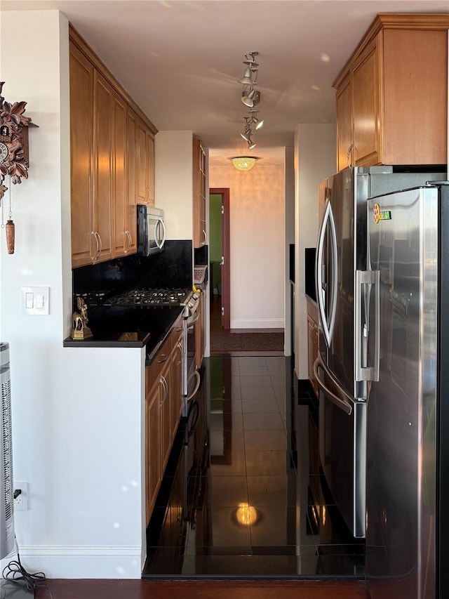 kitchen featuring dark stone countertops, stainless steel appliances, rail lighting, and dark tile patterned floors