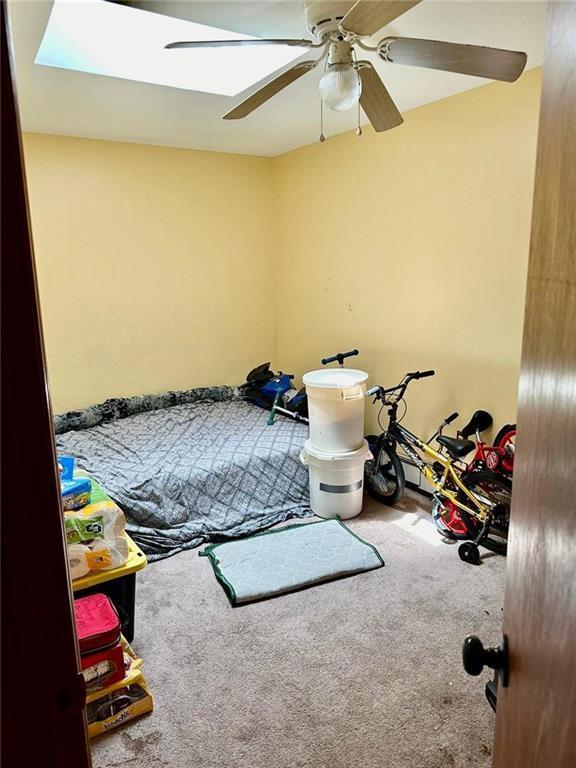 bedroom with ceiling fan, a skylight, and carpet flooring