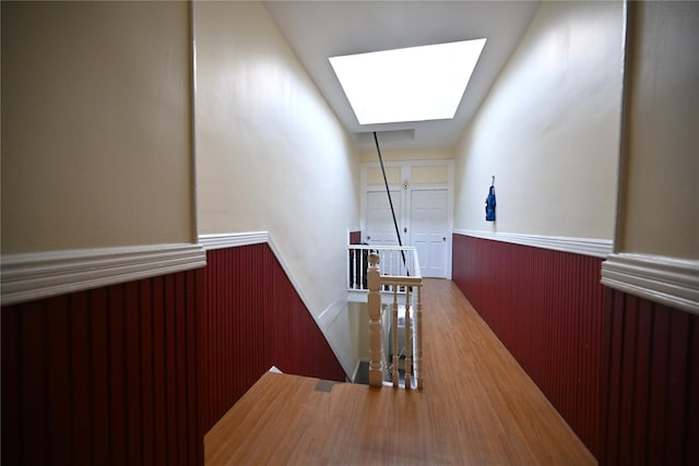 corridor featuring hardwood / wood-style flooring, wooden walls, and a skylight