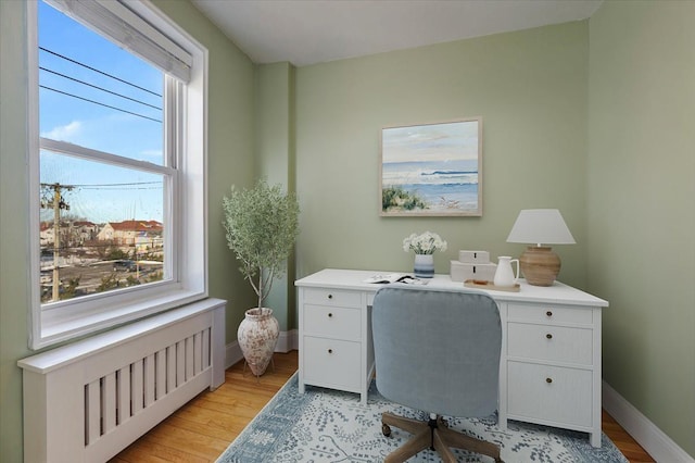 office area with light hardwood / wood-style flooring, radiator heating unit, and a wealth of natural light