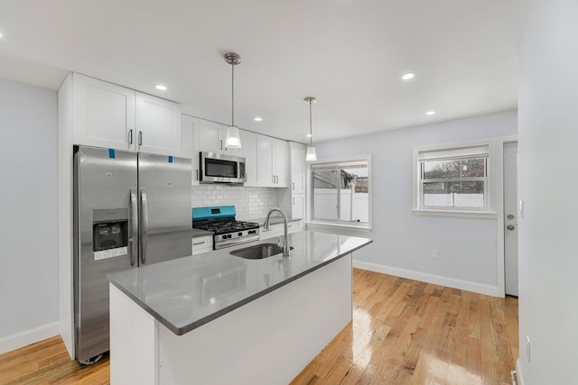 kitchen with white cabinets, appliances with stainless steel finishes, decorative light fixtures, an island with sink, and sink