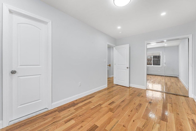 unfurnished bedroom with light wood-type flooring and a baseboard heating unit