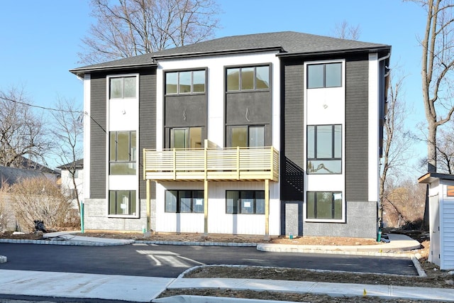 view of front facade featuring stucco siding, a balcony, and a shingled roof