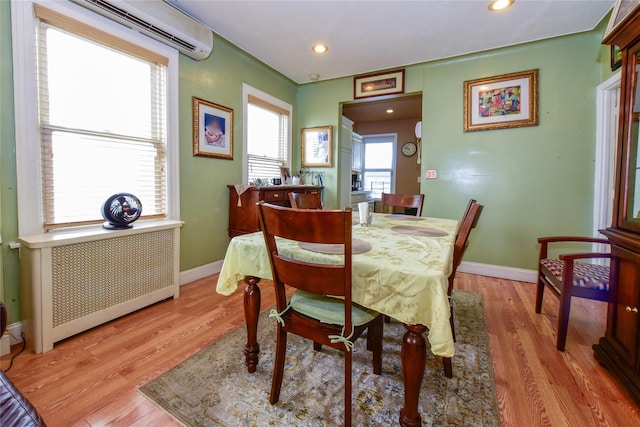 dining area featuring a wall mounted air conditioner, radiator heating unit, and light hardwood / wood-style floors