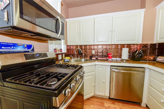 kitchen with stainless steel appliances, sink, white cabinets, and light hardwood / wood-style floors