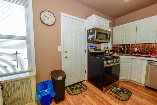 kitchen with radiator heating unit, white cabinetry, sink, stainless steel appliances, and light wood-type flooring