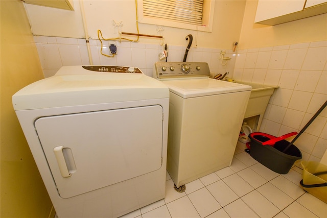 clothes washing area featuring light tile patterned flooring, independent washer and dryer, and tile walls