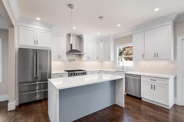 kitchen with wall chimney range hood, stainless steel appliances, white cabinetry, and hanging light fixtures