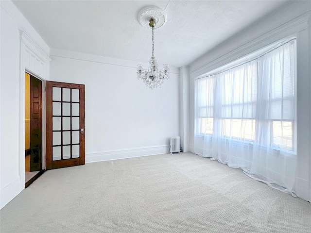 unfurnished room with crown molding, carpet floors, radiator heating unit, and a chandelier