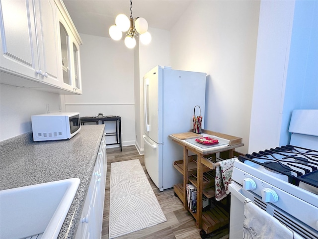 kitchen with sink, white appliances, white cabinets, decorative light fixtures, and light wood-type flooring