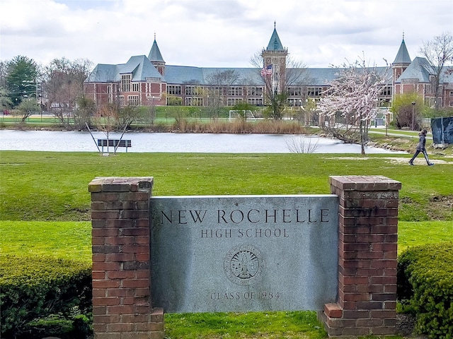 community sign featuring a water view and a yard