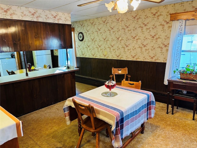 carpeted dining space with ceiling fan, a baseboard radiator, a drop ceiling, and stacked washer and dryer