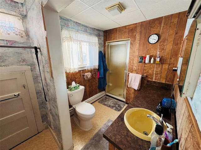 bathroom with a shower with shower door, toilet, a baseboard heating unit, vanity, and wood walls