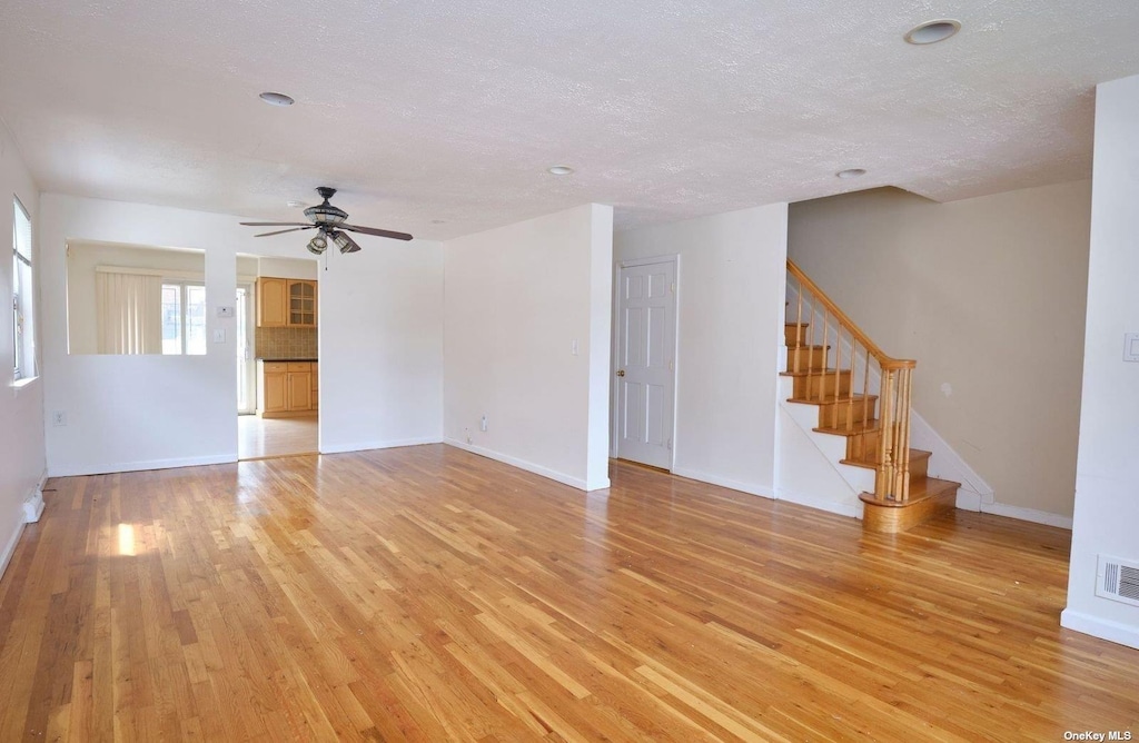 unfurnished living room with ceiling fan, light hardwood / wood-style flooring, and a textured ceiling