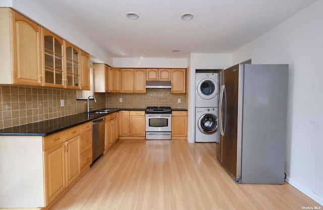 kitchen with sink, light wood-type flooring, tasteful backsplash, stacked washer and dryer, and stainless steel appliances