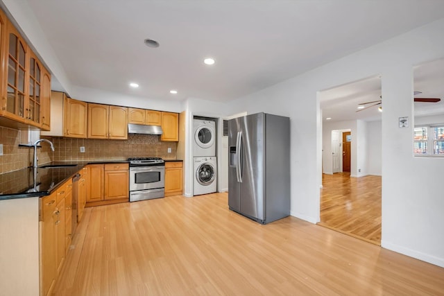 kitchen featuring sink, light hardwood / wood-style flooring, stainless steel appliances, stacked washer and clothes dryer, and tasteful backsplash