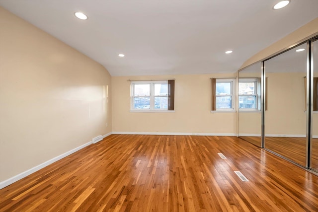 unfurnished bedroom featuring multiple windows, hardwood / wood-style floors, lofted ceiling, and a closet