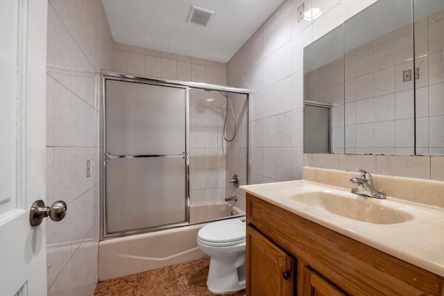 full bathroom with tile patterned floors, toilet, shower / bath combination with glass door, tile walls, and vanity