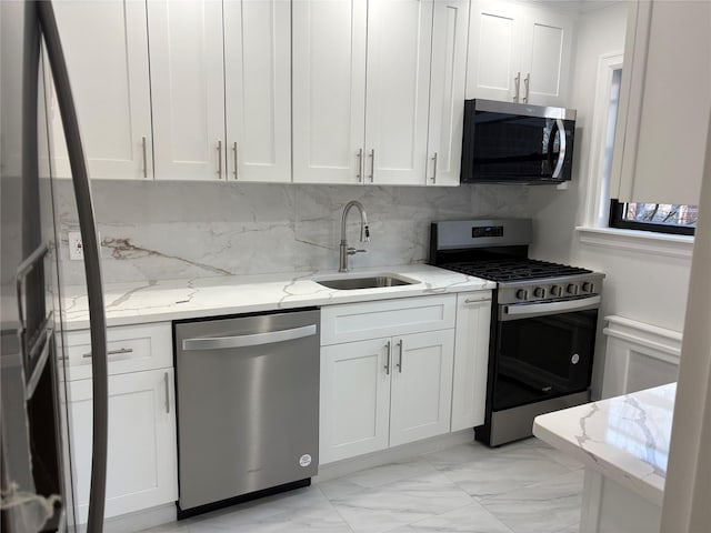 kitchen with light stone countertops, white cabinetry, stainless steel appliances, sink, and backsplash