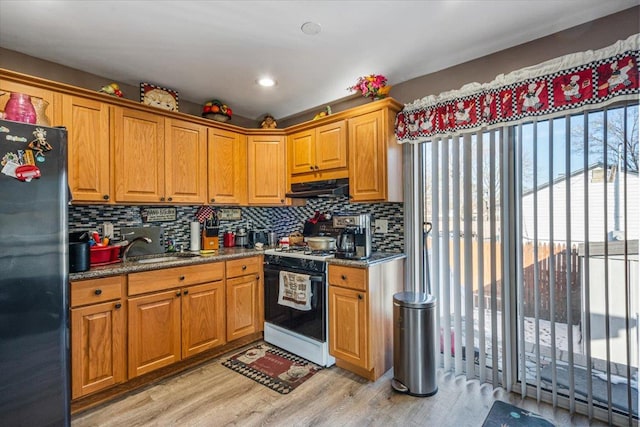 kitchen featuring tasteful backsplash, dark stone counters, white gas range oven, black fridge, and light wood-type flooring