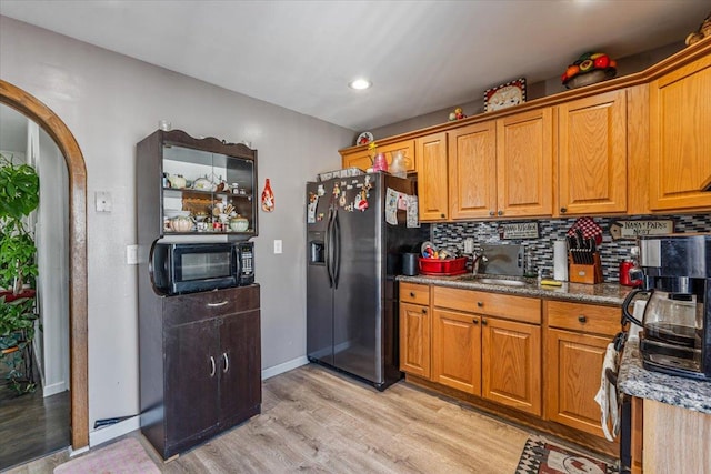 kitchen featuring sink, backsplash, stainless steel refrigerator with ice dispenser, light hardwood / wood-style floors, and dark stone counters