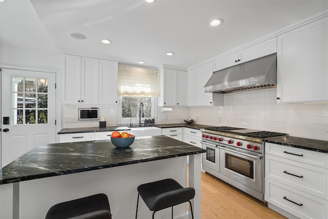 kitchen with a healthy amount of sunlight, a breakfast bar, double oven range, and range hood