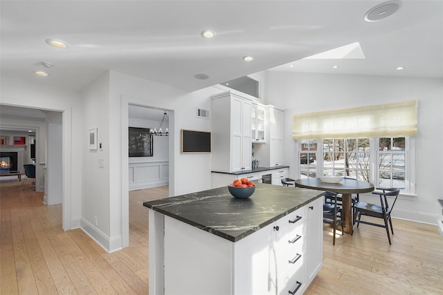 kitchen with light hardwood / wood-style flooring, lofted ceiling with skylight, white cabinets, a kitchen island, and dark stone counters