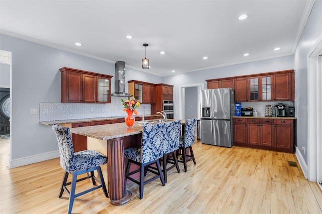 kitchen featuring crown molding, wall chimney range hood, decorative light fixtures, and appliances with stainless steel finishes