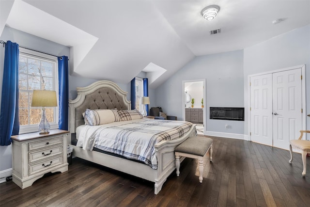 bedroom with lofted ceiling, dark hardwood / wood-style floors, connected bathroom, and a closet