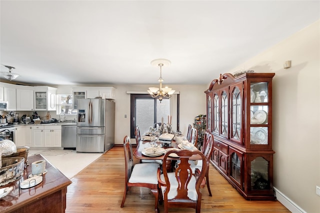 dining space with sink, light hardwood / wood-style floors, and a notable chandelier