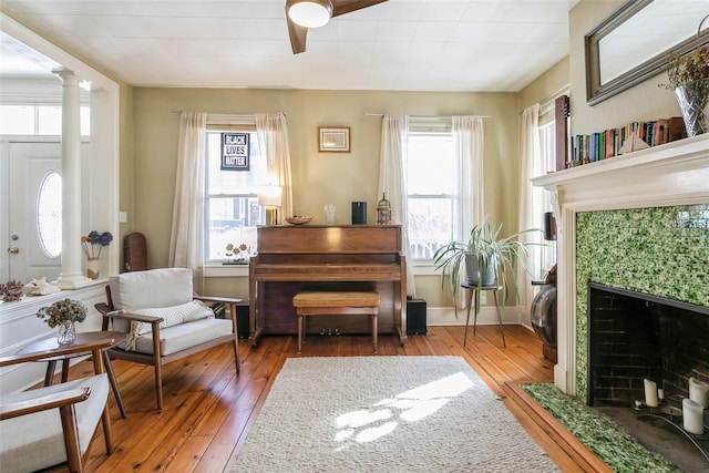 living area with decorative columns, wood-type flooring, and a tiled fireplace