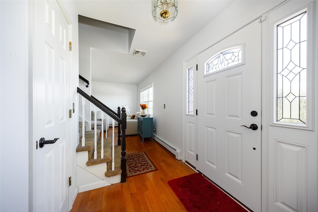 entrance foyer featuring a baseboard radiator, wood finished floors, visible vents, baseboards, and stairway