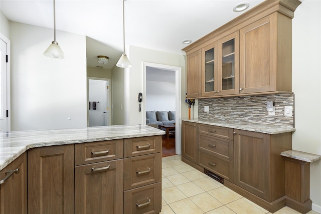 kitchen featuring hanging light fixtures, light stone countertops, glass insert cabinets, and decorative backsplash